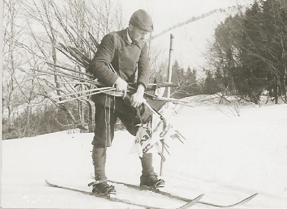 Historická fotografia muža na lyžiach s lyžiarskymi palicami na snehu.