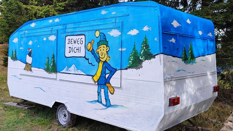 Farebne namaľovaný karavan so zimnou krajinou a postavou s nápisom "Hýbte sa!".