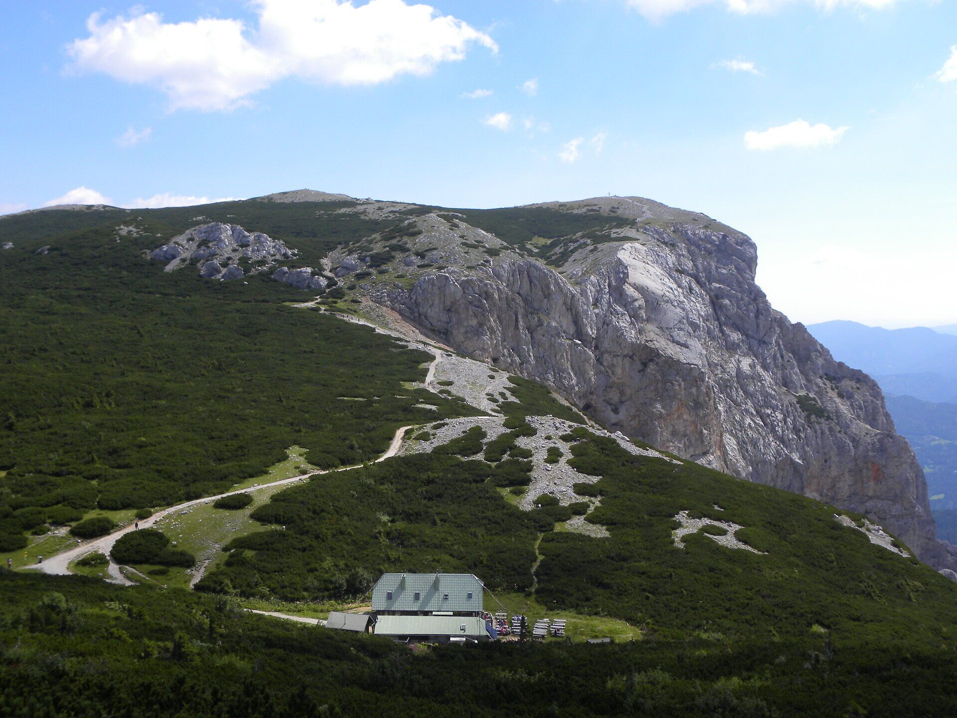 Horská krajina na Raxe s nápadnými skalnými útvarmi, turistickými chodníkmi a horskou chatou pod modrou oblohou.