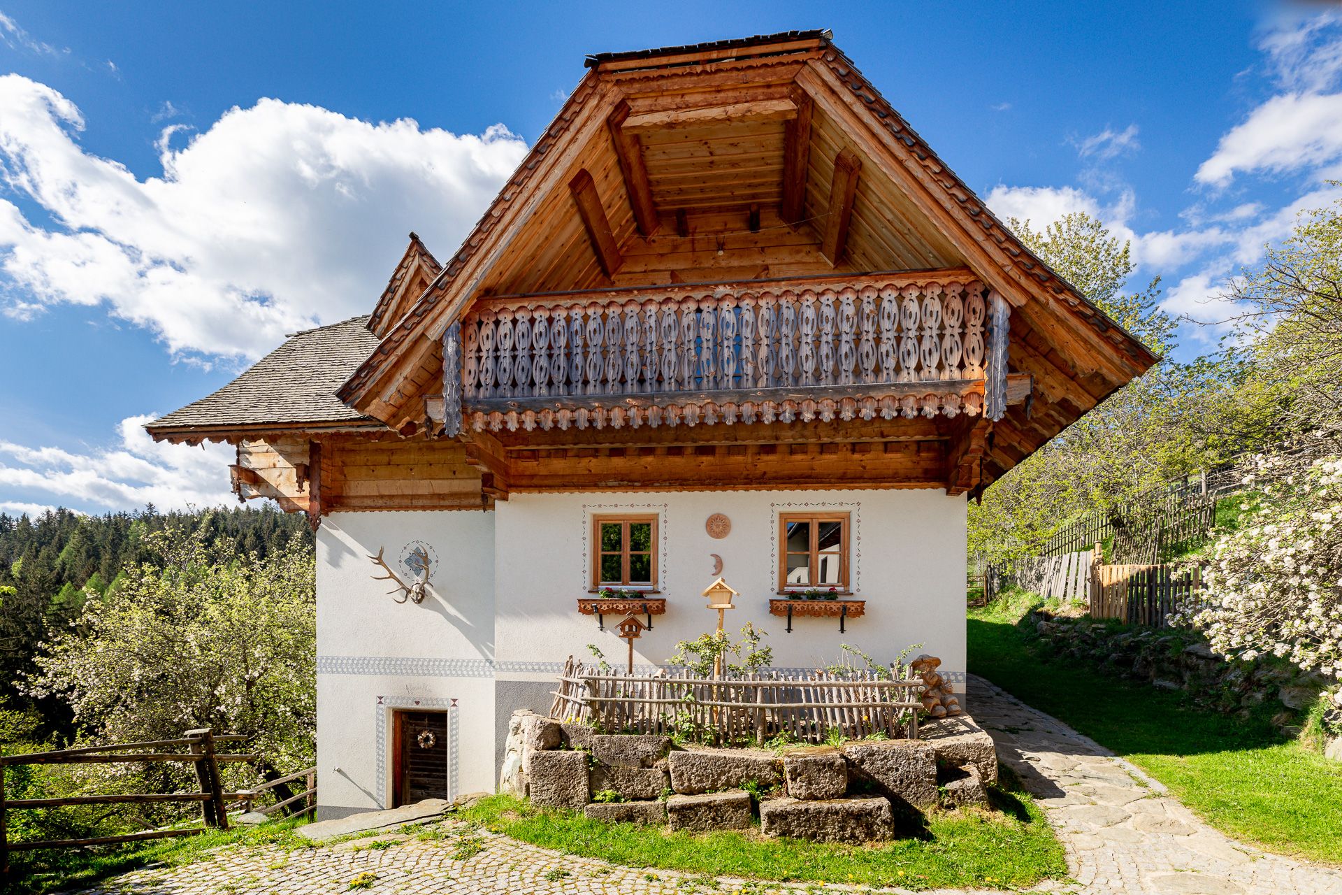 Tradičný dom s dreveným balkónom a bielou fasádou, obklopený prírodou.