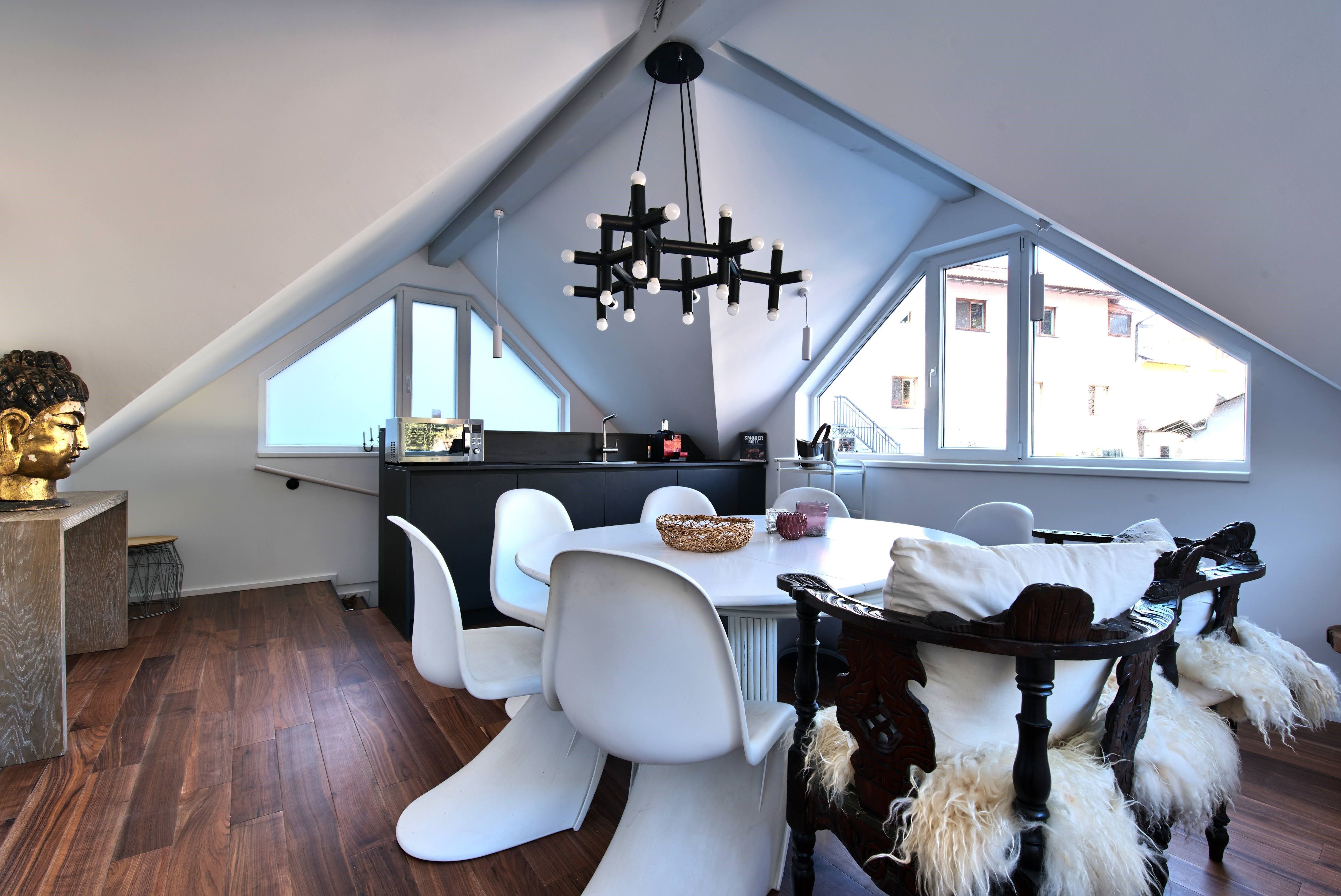 Moderný jedálenský kút v podkroví s bielymi stoličkami, drevenou podlahou a veľkým oknom.