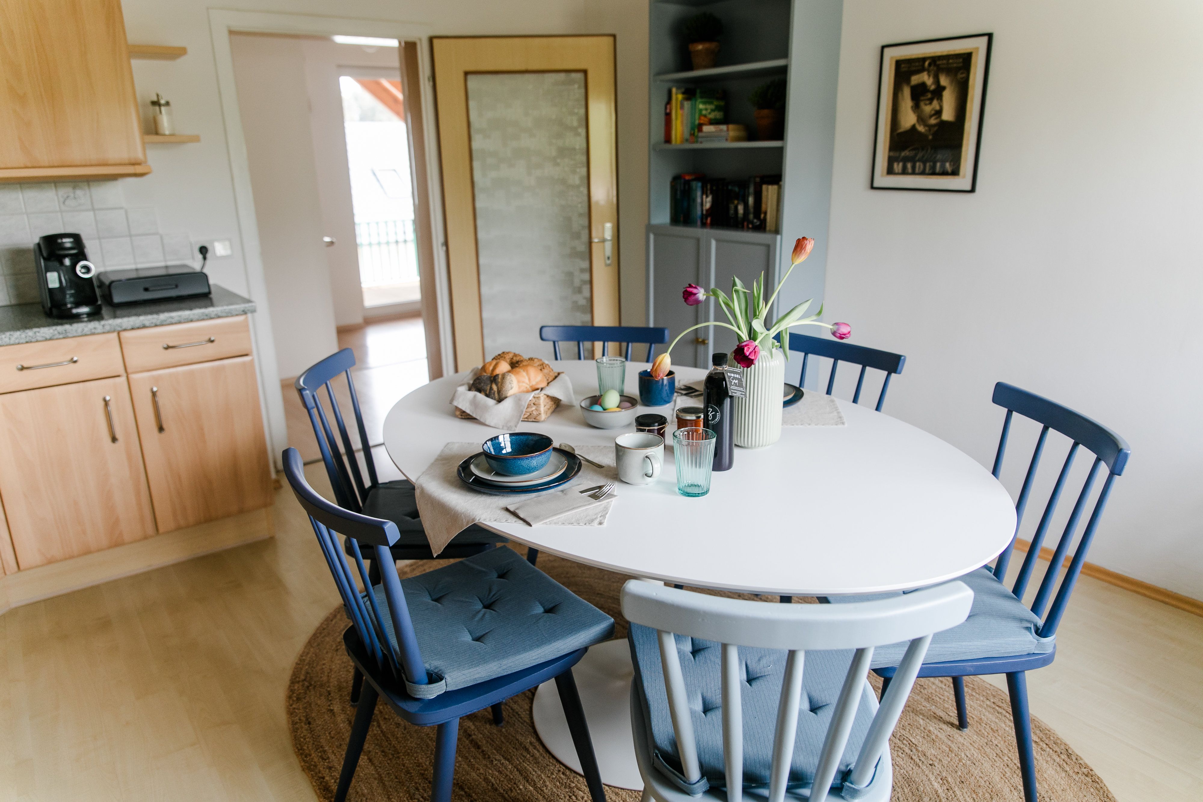 Jedálenský kút v kuchyni s okrúhlym stolom, modrými stoličkami a raňajkovým stolom.