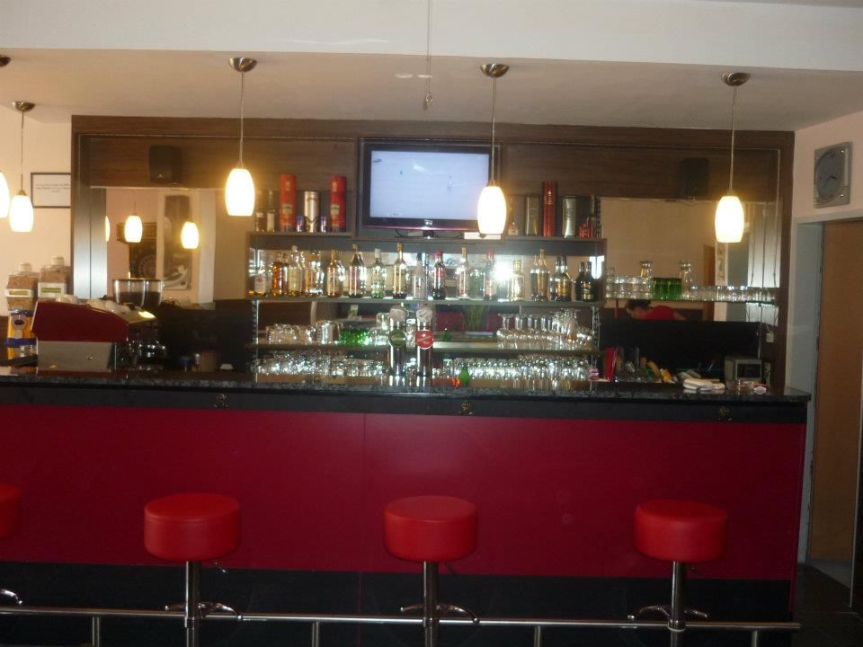 Pohľad do interiéru baru s červenými stoličkami a osvetlenými policami plnými fliaš.