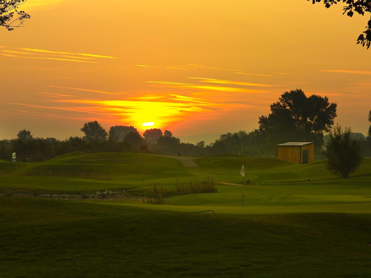 Západ slnka nad golfovým ihriskom s vlajkou a malou budovou.