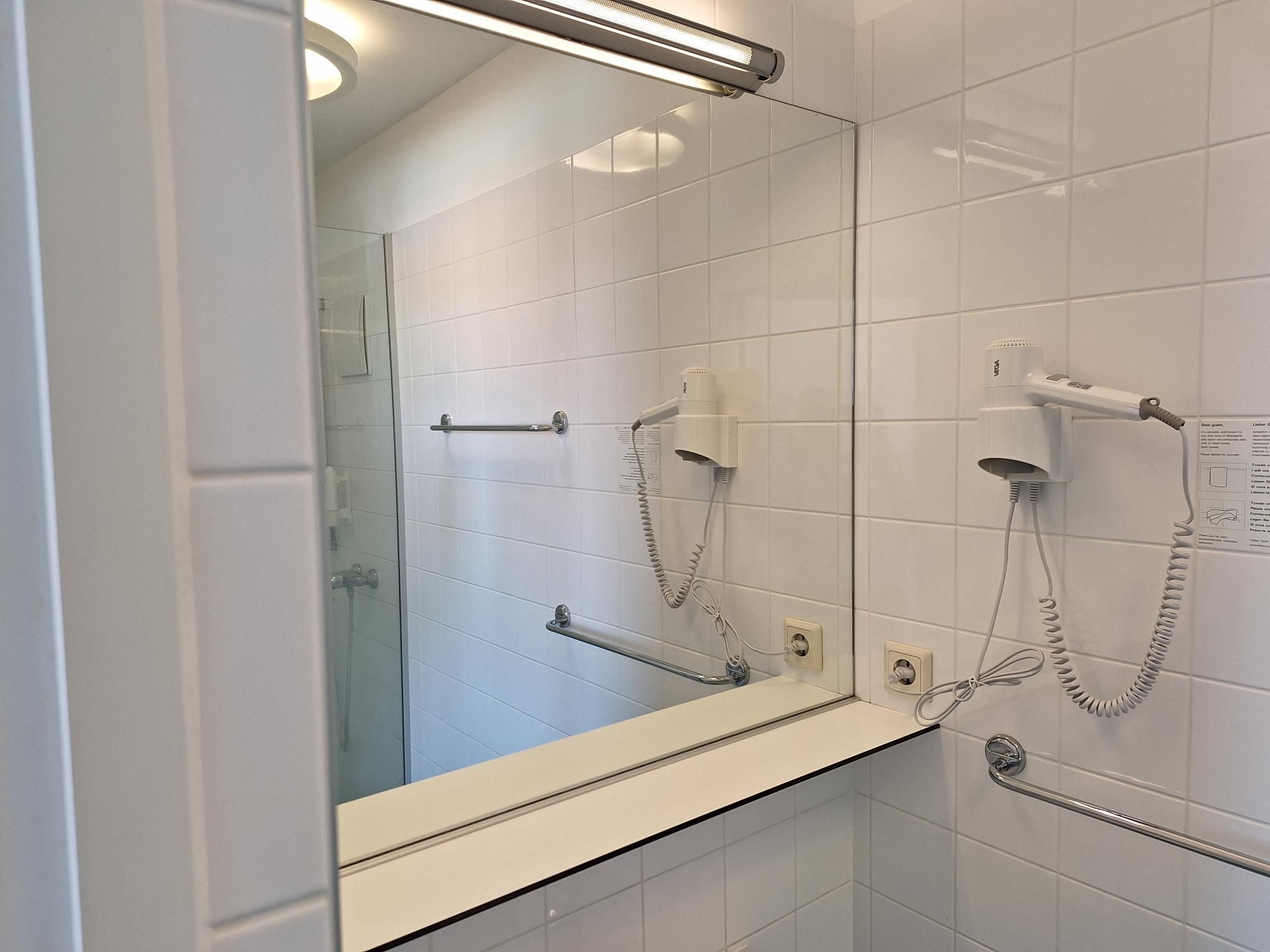 Moderná kúpeľňa so zrkadlom, sušičom vlasov a vešiakom na uteráky.