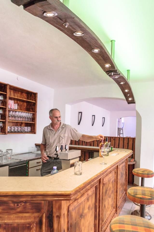 Muž stojí za dreveným barom vo vínnej pivnici a nalieva víno.