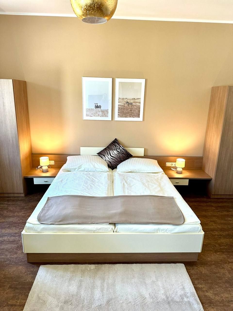 Moderná spálňa s manželskou posteľou, dvoma nočnými stolíkmi a nástennými maľbami.