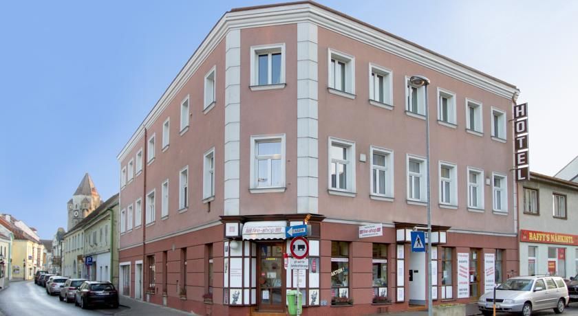 Trojposchodová budova hotela na rohu ulice s autami a obchodmi.