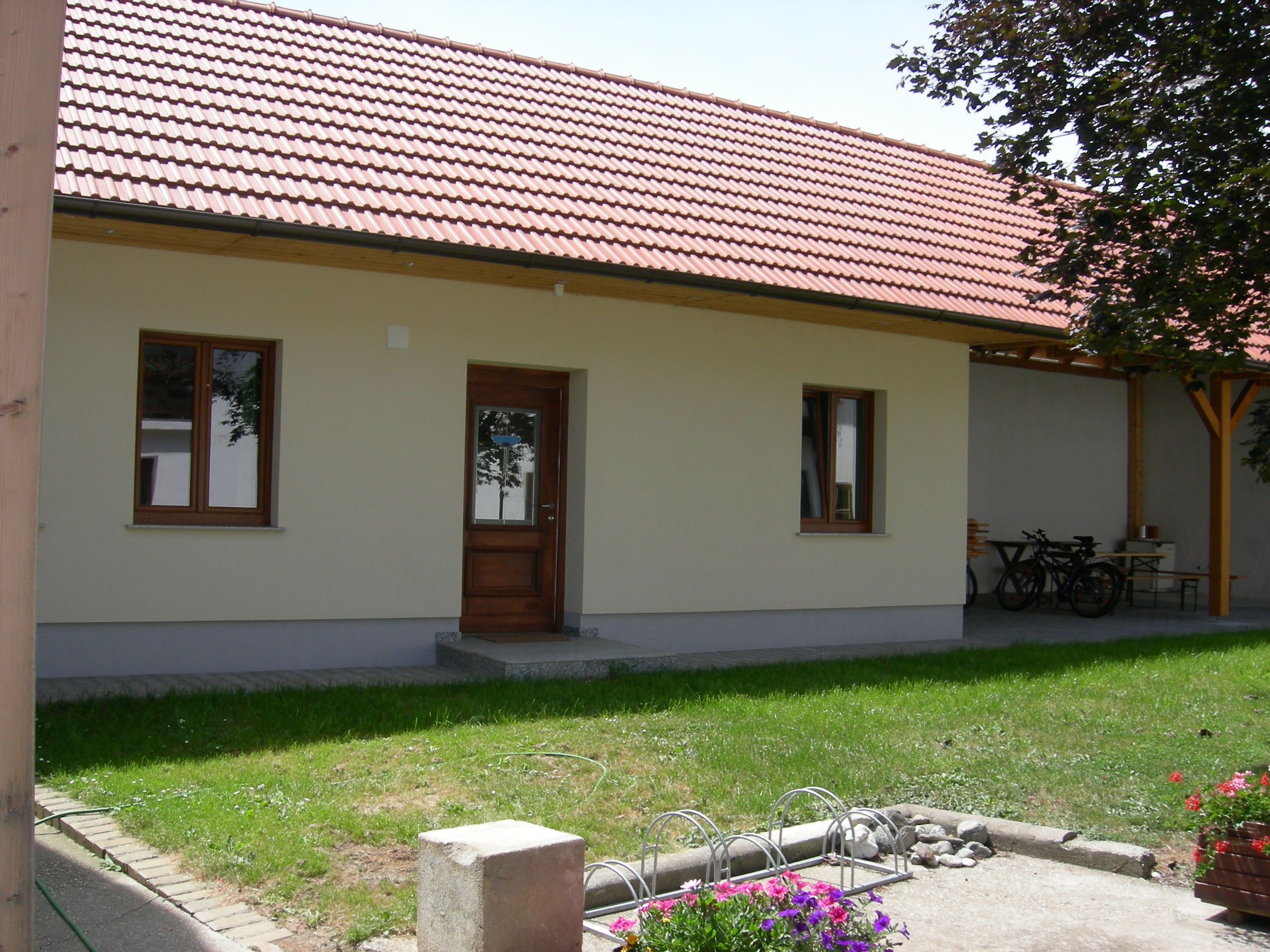 Vnútorný dvor s budovou s červenou škridlovou strechou, drevenými dverami a oknami. V popredí vidieť kvety a stojan na bicykle.