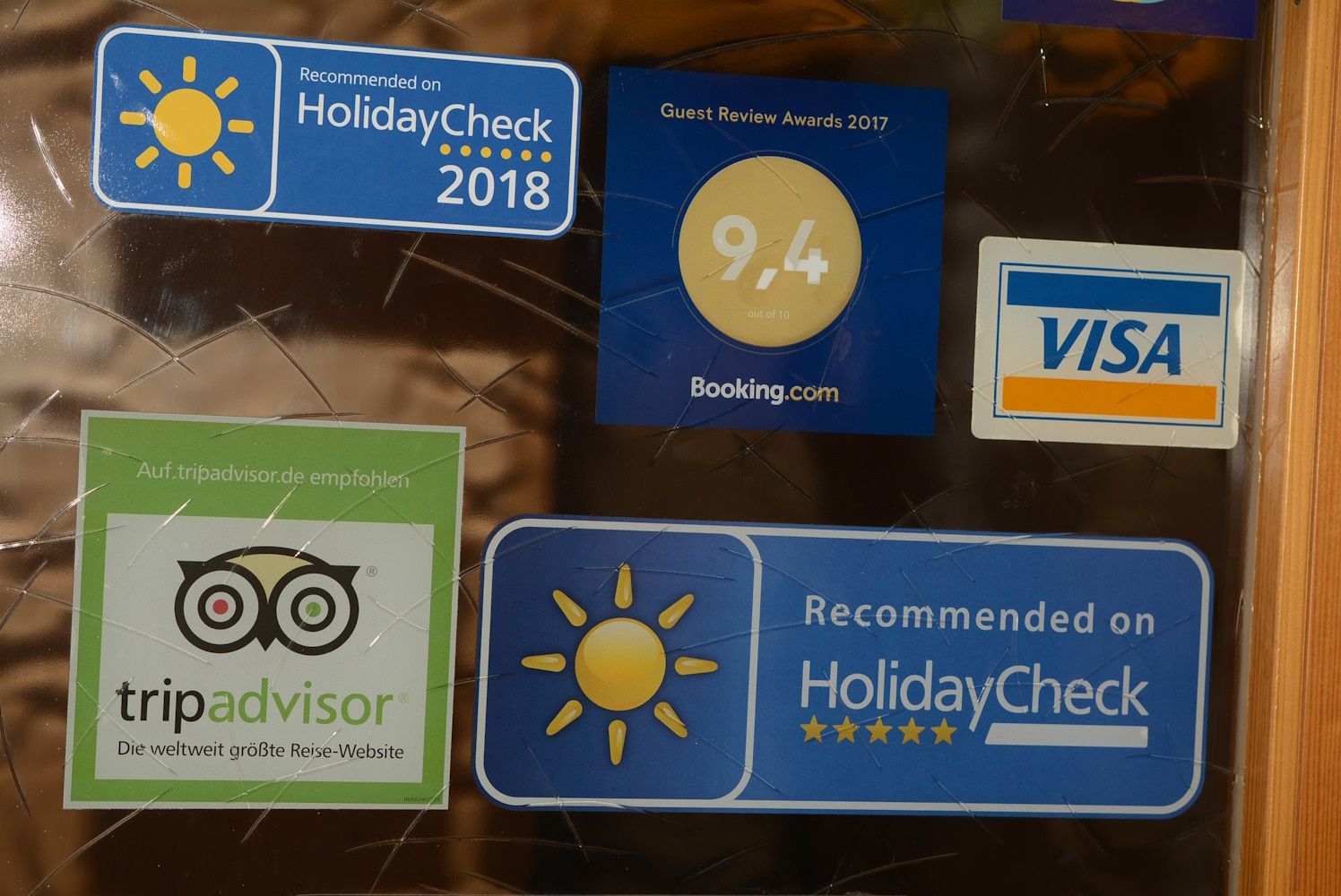 Nálepky od spoločností HolidayCheck, Booking.com, TripAdvisor a Visa na sklenenom povrchu.