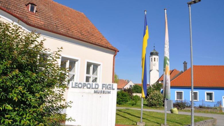 Leopold Figl Museum mit Fahnen und Kirchturm im Hintergrund.