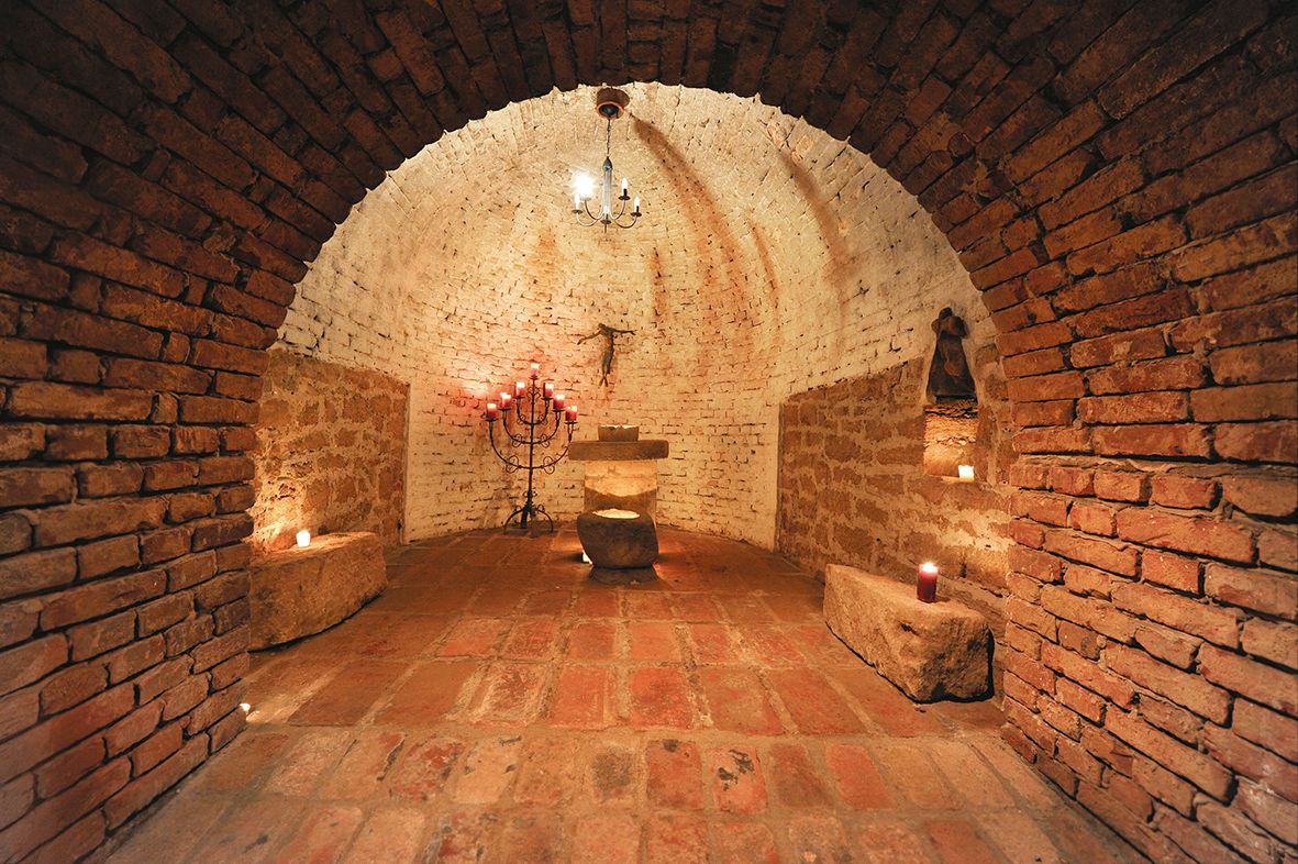 Rustikálna klenutá pivničná miestnosť so sviečkami a oltárom.