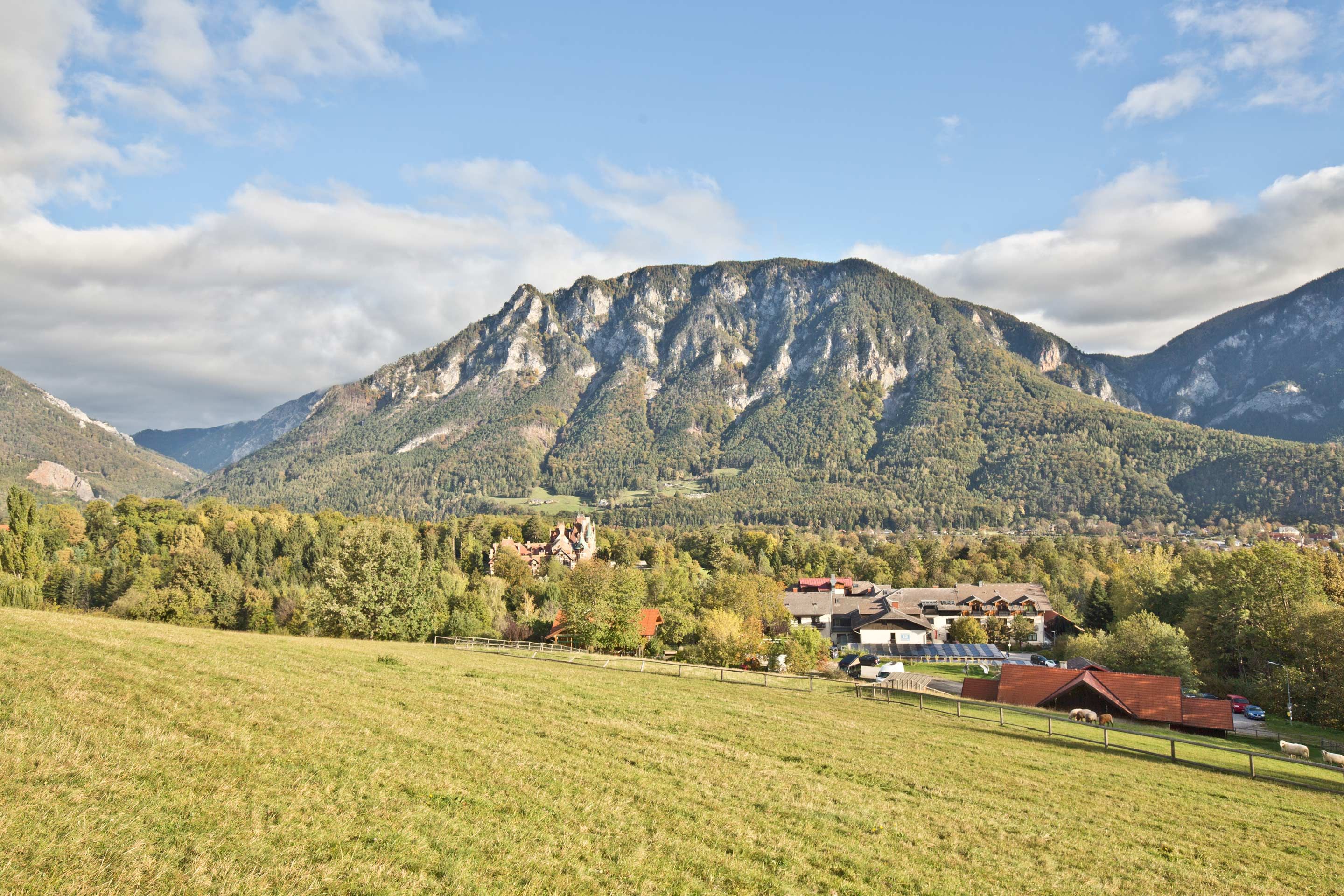 Panoramatický výhľad na horskú krajinu s lúkami v popredí a dedinou v pozadí.