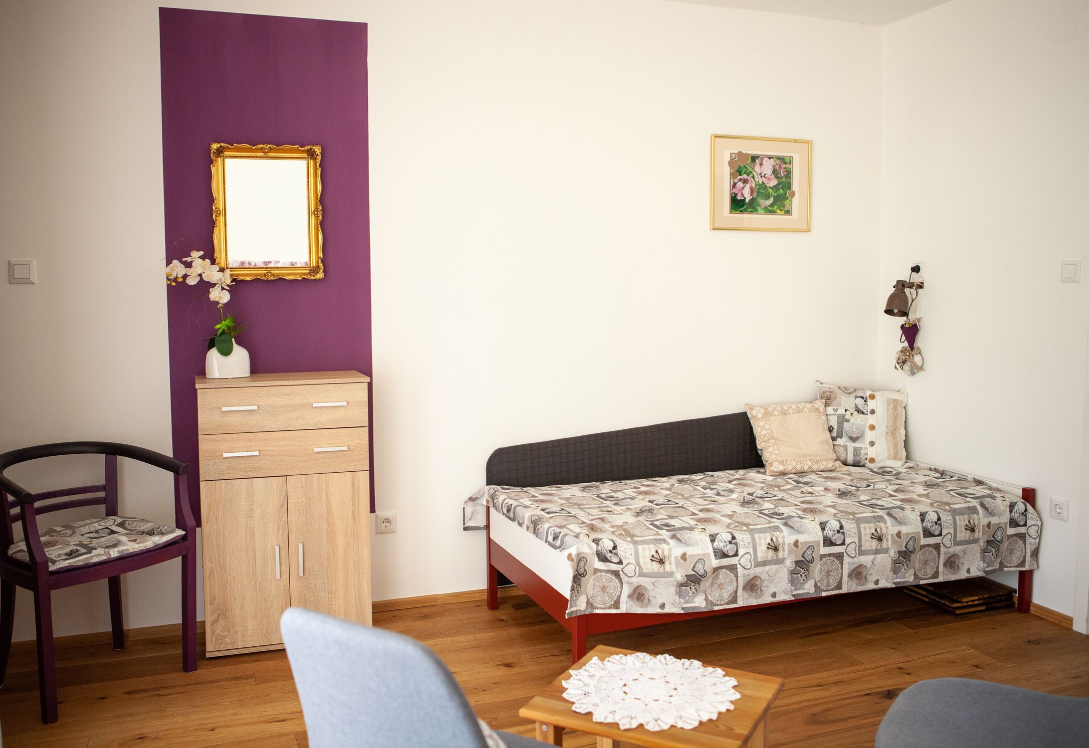 Obývacia izba s rozkladacou pohovkou, malou šatníkovou skriňou, stoličkou a stolom na drevenej podlahe.