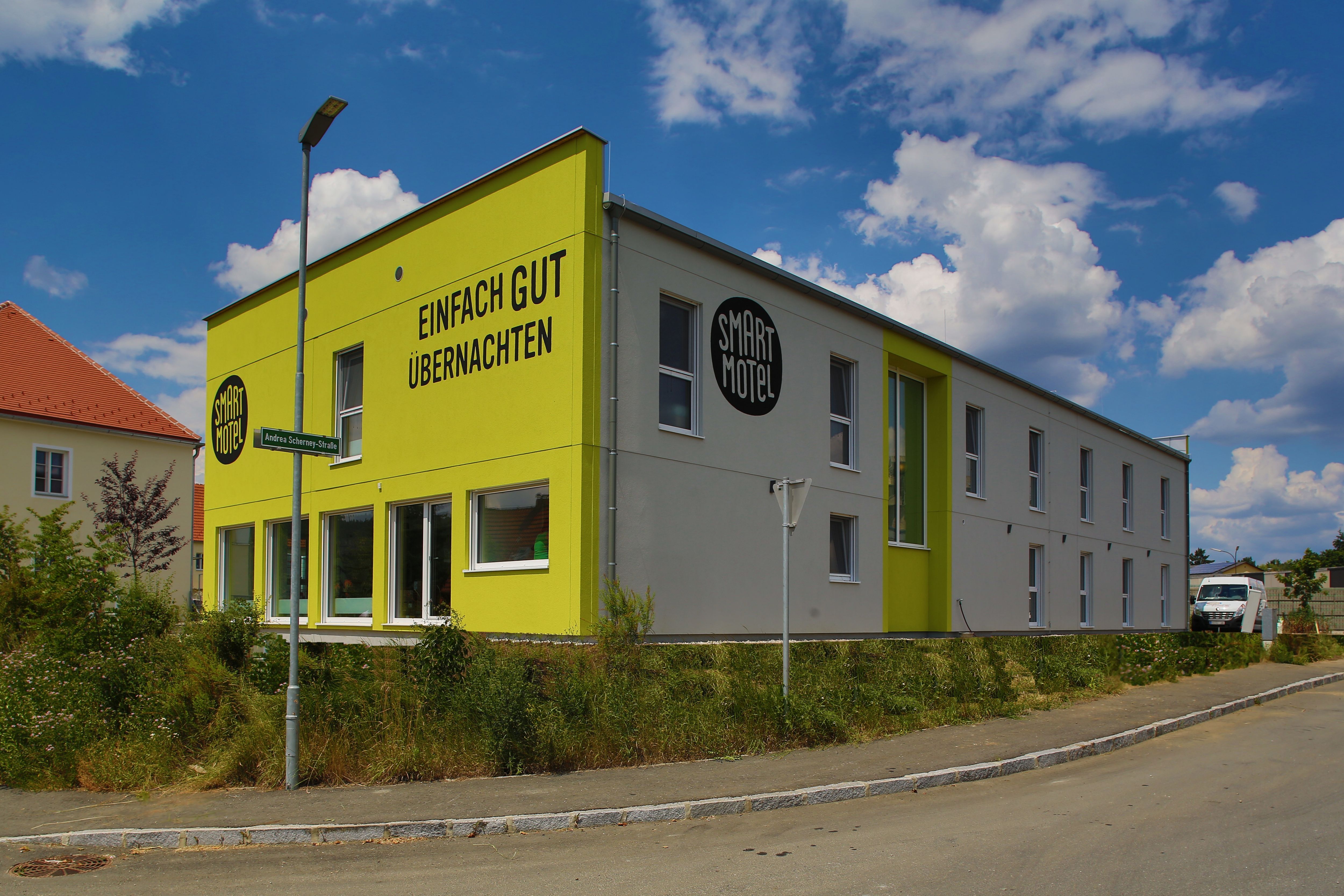 Pohľad zvonku na moderný dvojposchodový motel so žltou fasádou a nápisom "Einfach gut übernachten".
