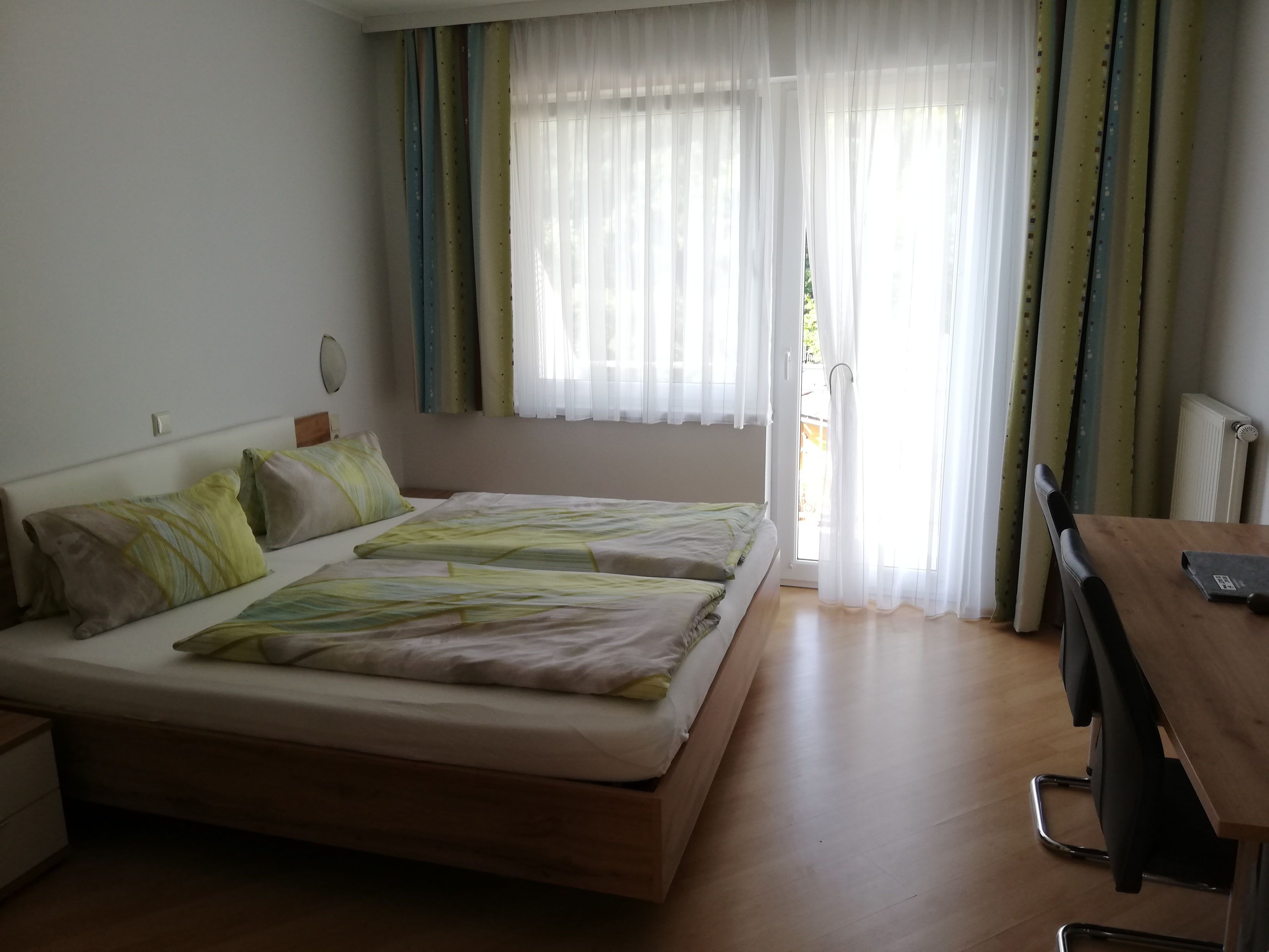 Dvojlôžková izba s posteľou, stolom a balkónom so závesmi.