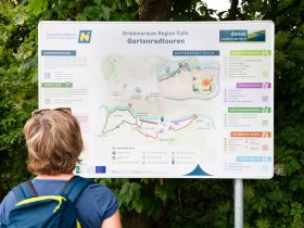 Osoba si prezer&aacute; informačn&uacute; tabuľu o z&aacute;hradn&yacute;ch cyklot&uacute;rach v Regione Tulln v Dolnom Rak&uacute;sku s mapou a inform&aacute;ciami o r&ocirc;znych tras&aacute;ch.