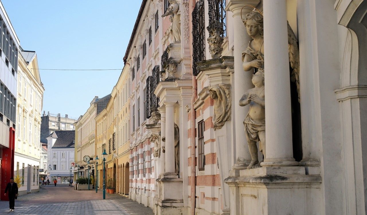 Ulica s historickými budovami a sochami v meste.