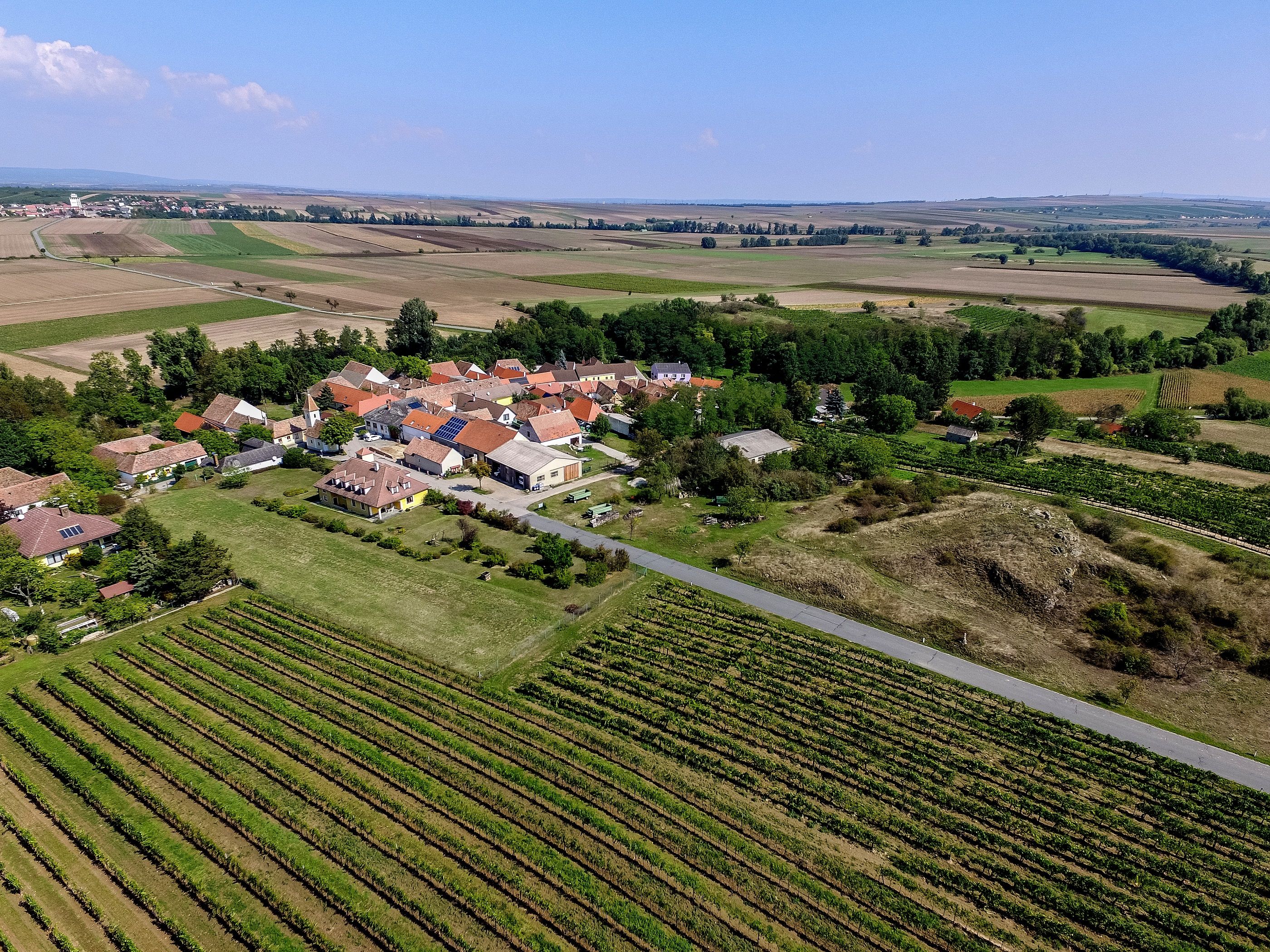 Letecký pohľad na malú dedinu obklopenú poliami a vinicami.