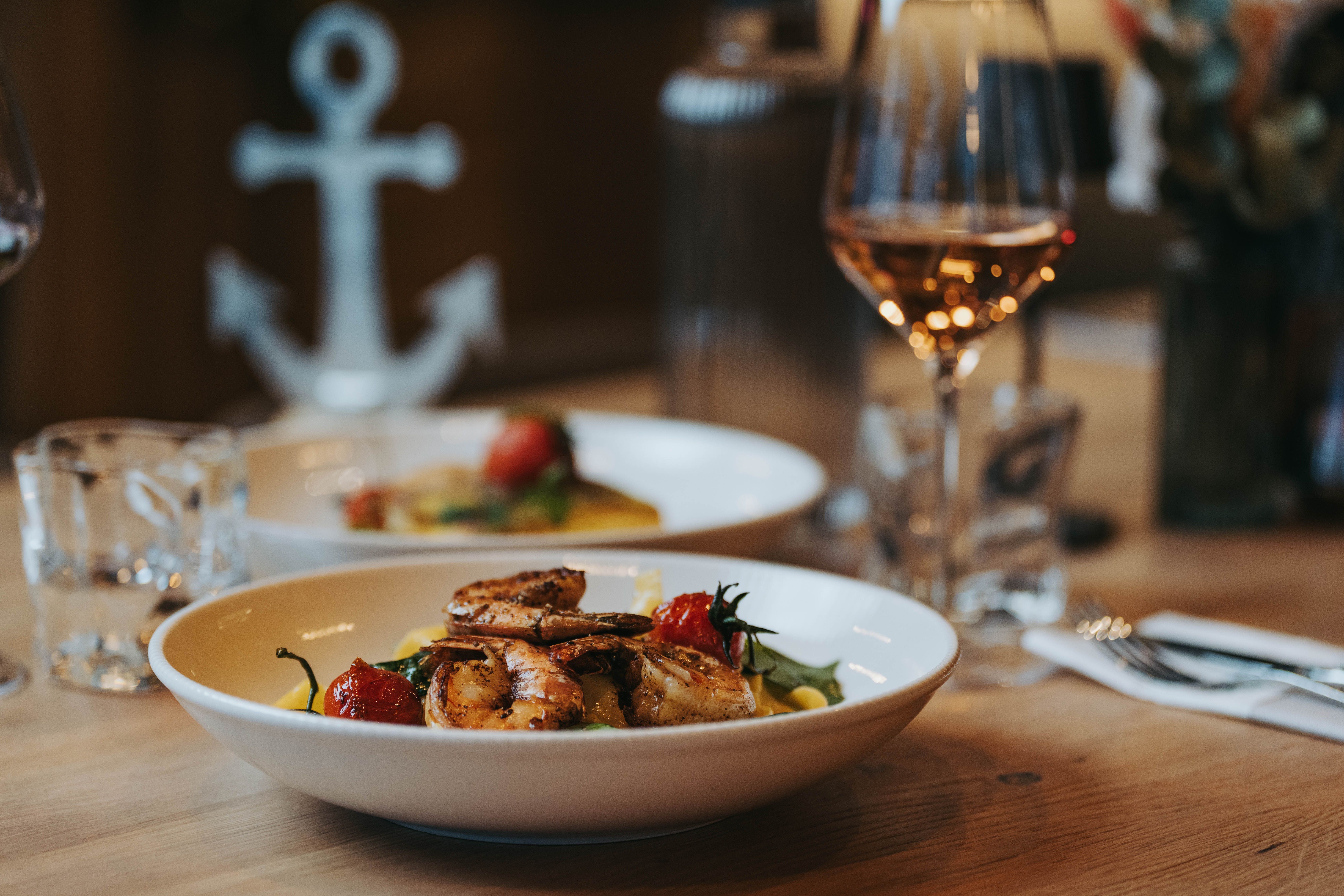 Na stole je tanier s krevetami a zeleninou a vedľa neho pohár vína.