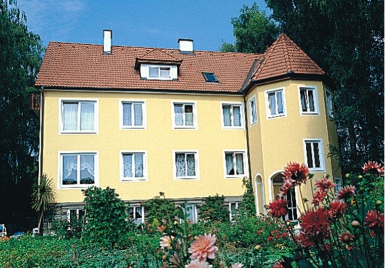 Žltý dom s červenou strechou a záhradou v popredí.