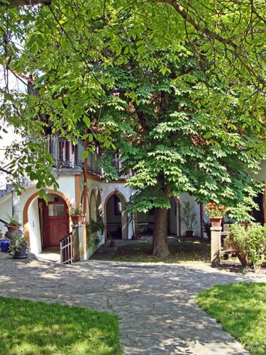 Idylické nádvorie s veľkým stromom, obklopené budovou s arkádami a balkónmi.