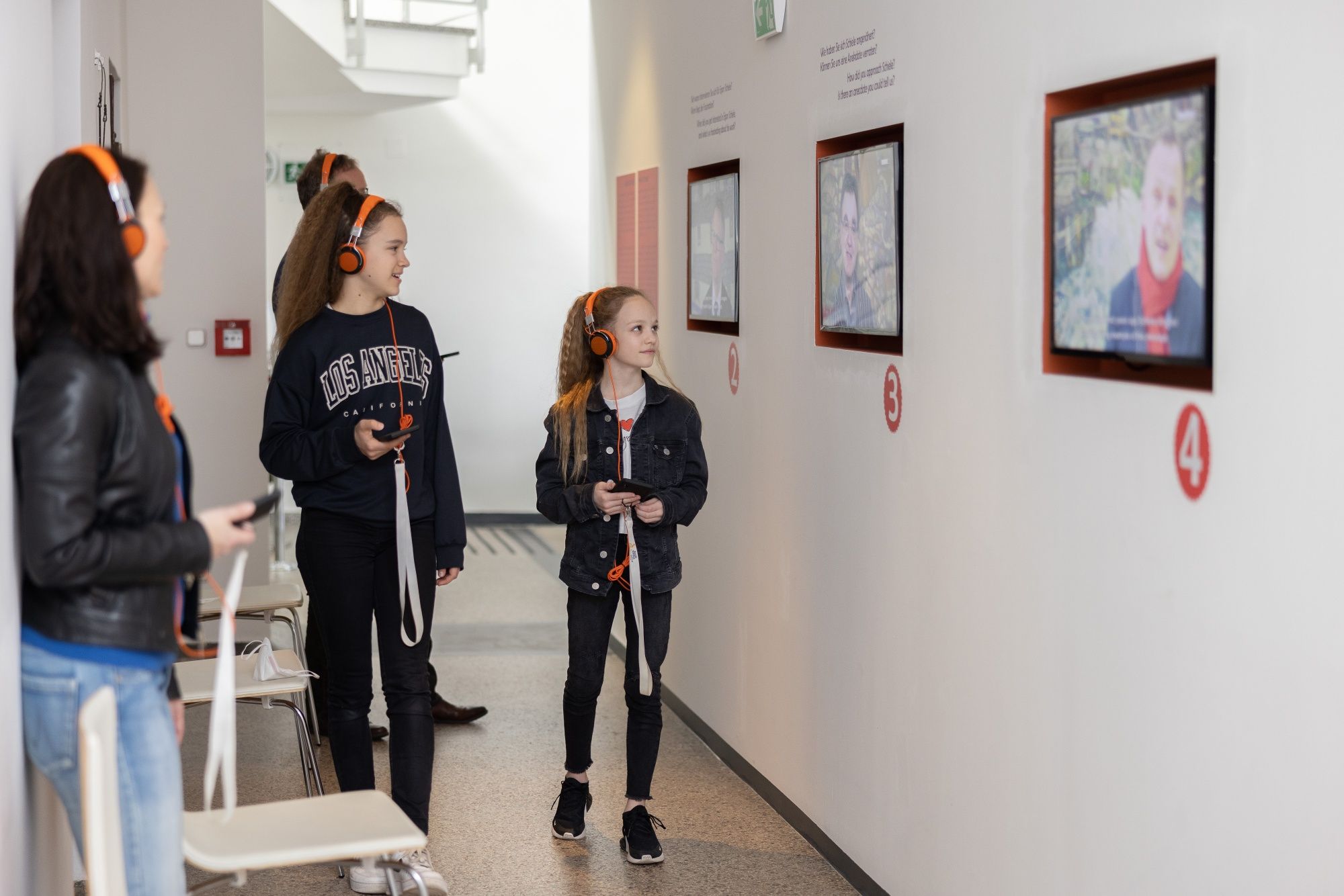 Návštevníci so slúchadlami sledujú obrazovky v múzeu.