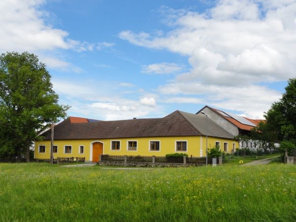 Žltá farma na zelenej lúke s modrou oblohou a mrakmi.