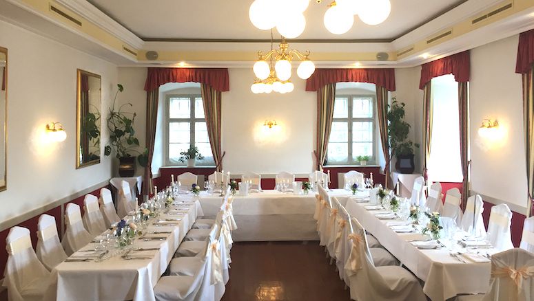 Elegantná sála na zámku Gloggnitz, vyzdobená na hostinu bielymi obrusmi a stoličkami.