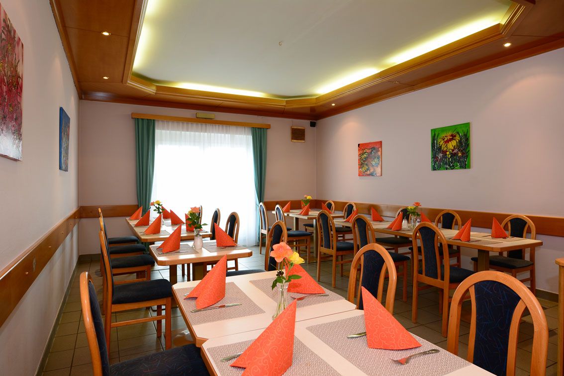 Jedáleň s prestretými stolmi, oranžovými obrúskami a vázami s kvetmi.