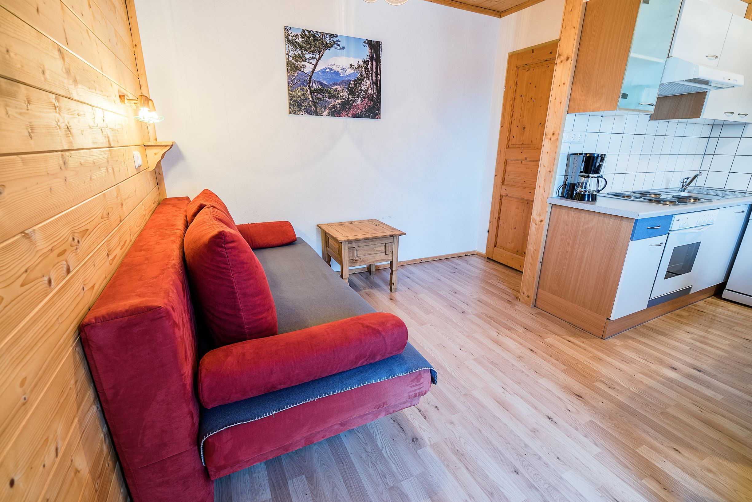 Obývacia izba s červenou pohovkou, drevenými stenami a malou kuchynkou.