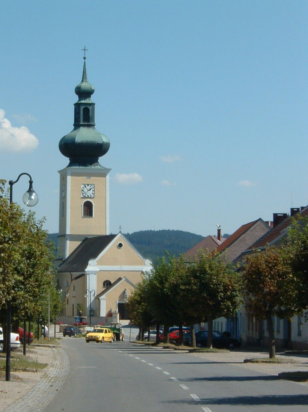 Kostol s cibuľovou kupolou v malom mestečku, obklopený stromami a domami.