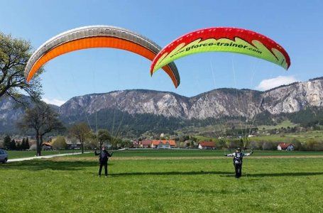 Dvaja ľudia cvičia paragliding na lúke pred horskou krajinou.