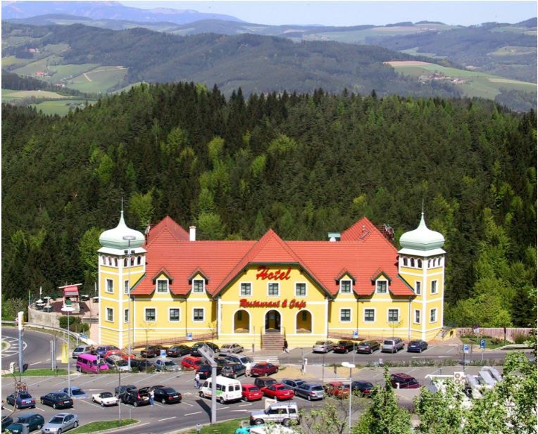 Žltý hotel s červenými strechami v zelenej kopcovitej krajine.