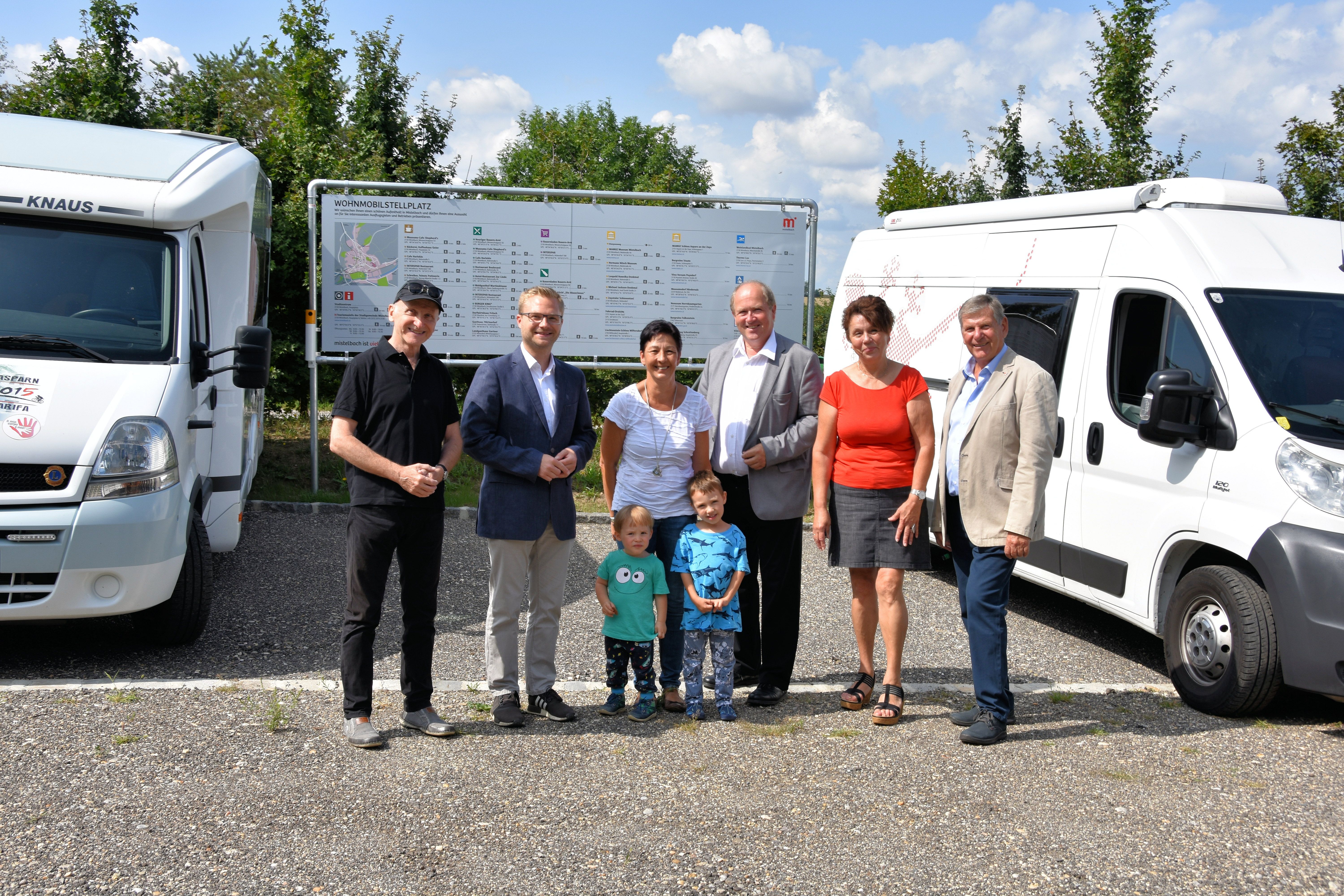 Skupina ľudí pred karavanmi a nápis na ihrisku.