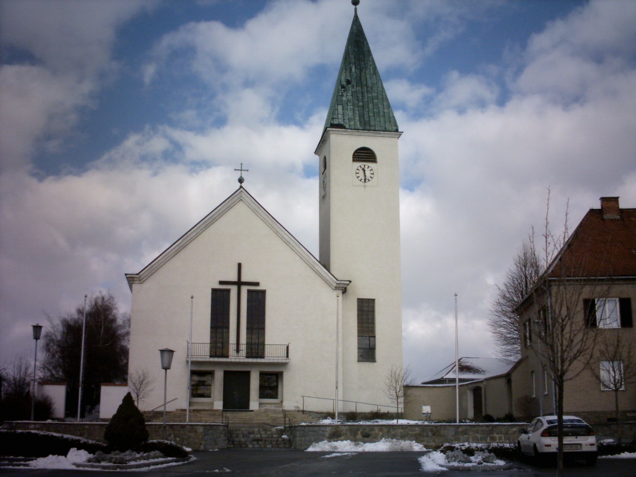 Kostol s vežou a hodinami v Sigmundsherbergu, obklopený snehom a mrakmi.