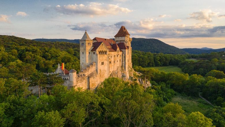 Lichtenštajnský hrad obklopený zelenými lesmi pri západe slnka.