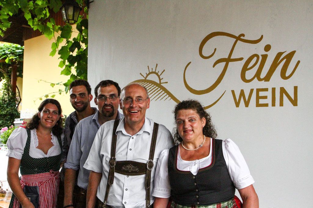 Skupina piatich ľudí v tradičnom odeve pred nápisom "Fein Wein".