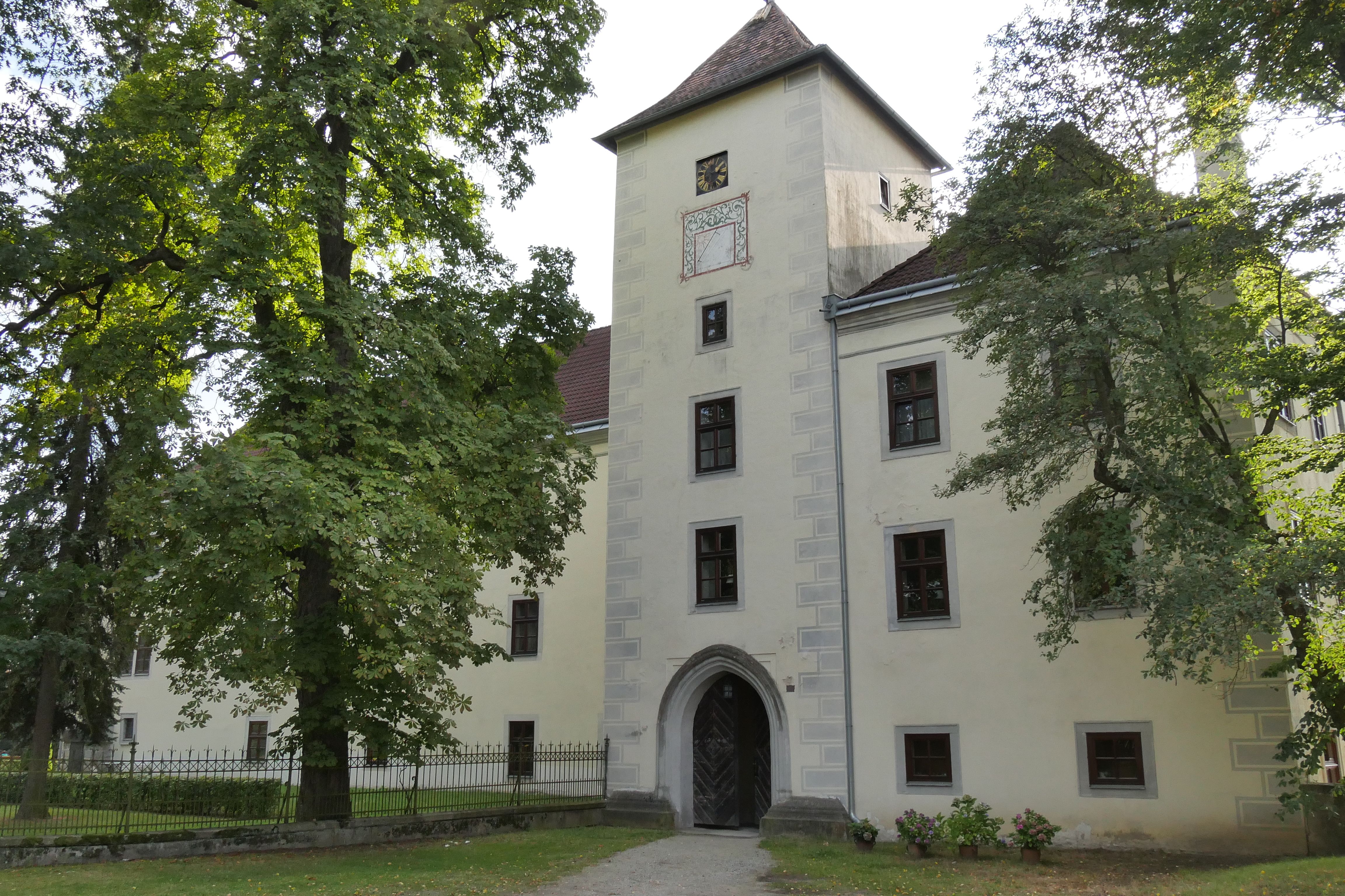 Historická budova s vežou a stromami v popredí.