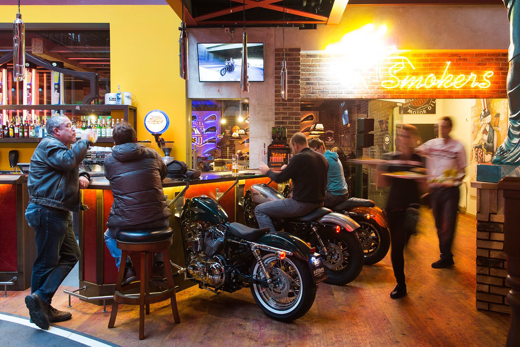Bar s motorkami ako sedadlami, neónovým svetlom a hosťami.