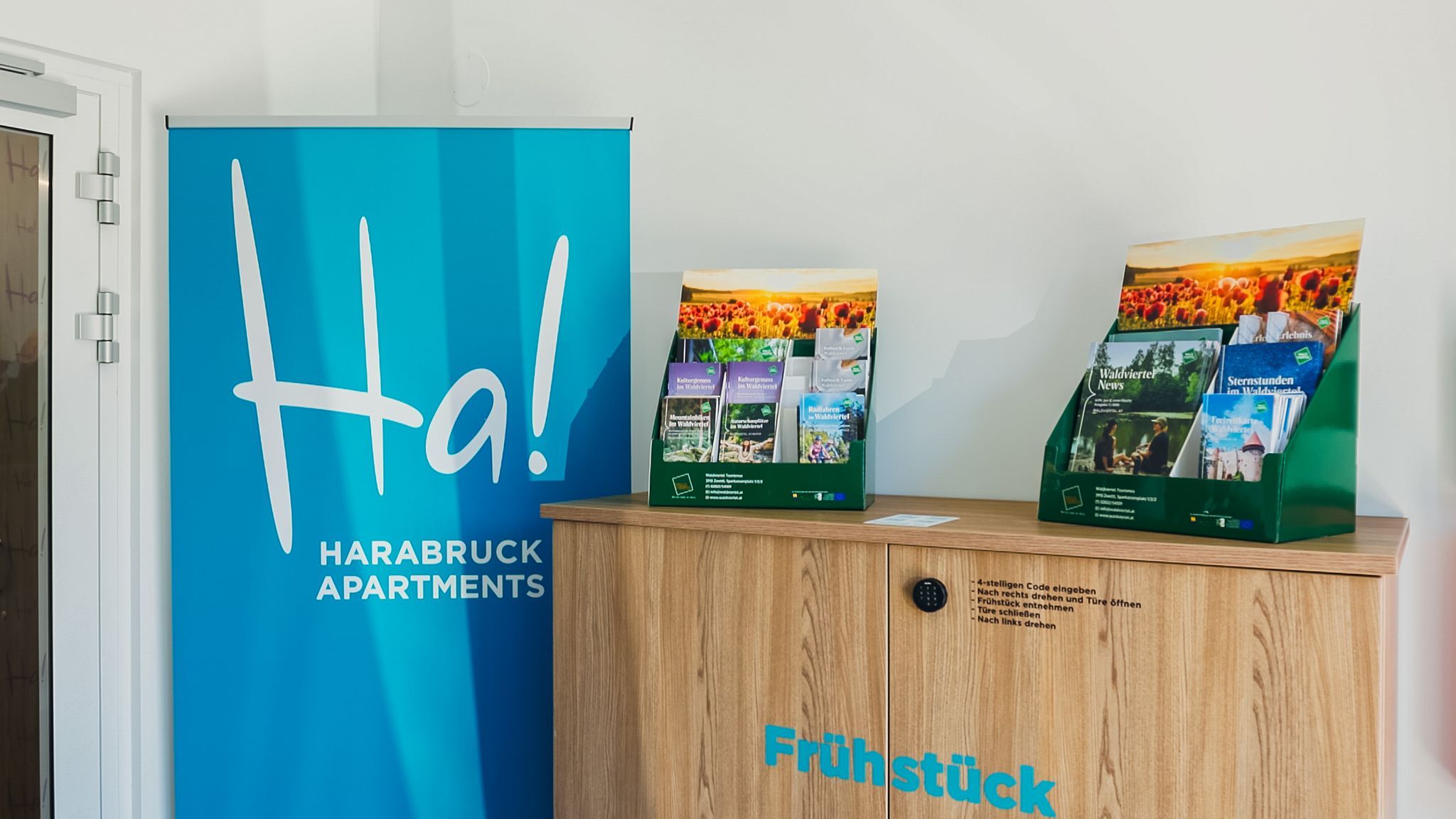 Recepcia s modrým nápisom „Harabruck Apartments“ a stojanom na prospekty umiestneným na drevenej skrinke.