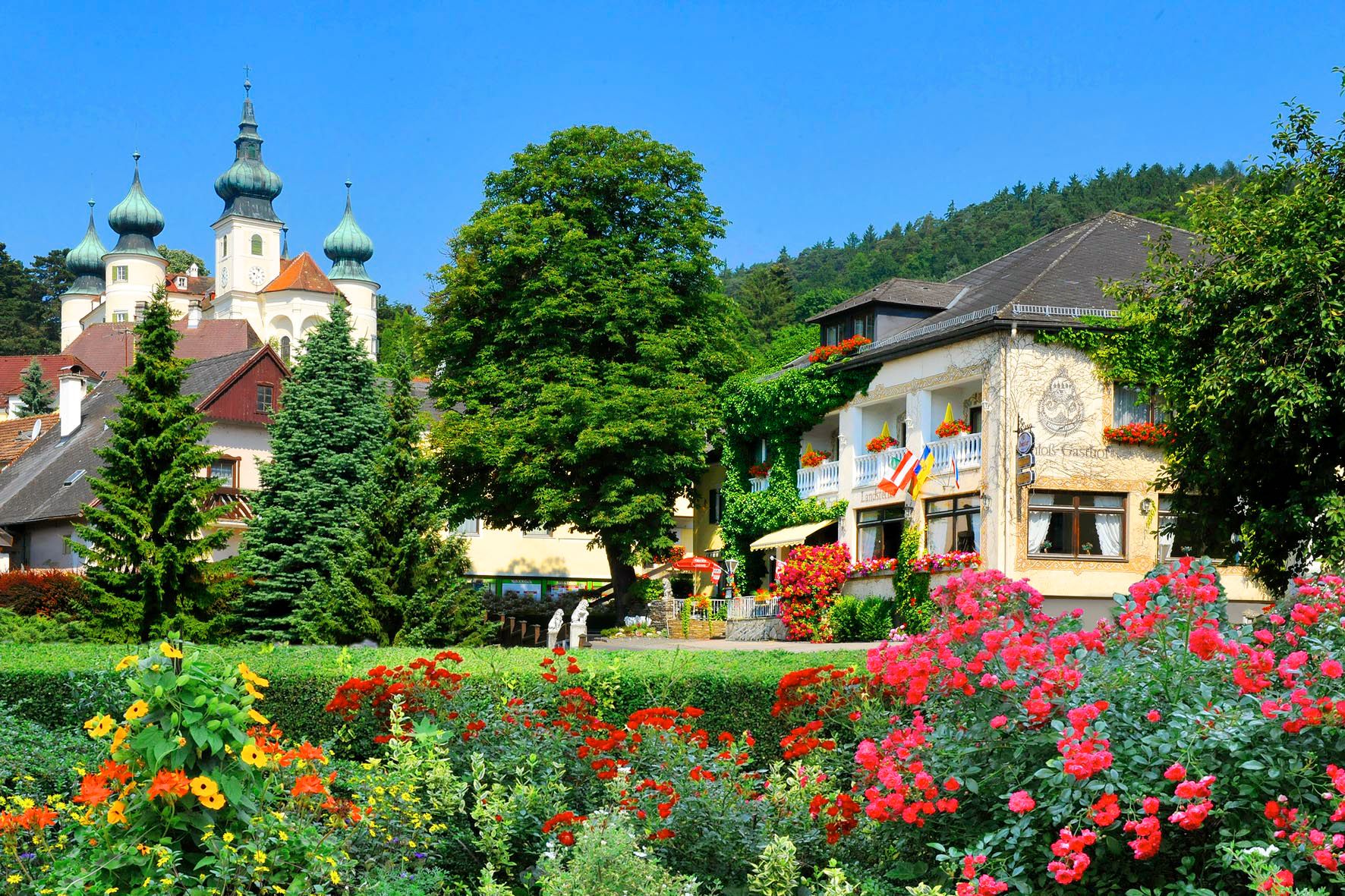 Malebný hotel s farebnými kvetmi v popredí a hradom v pozadí.