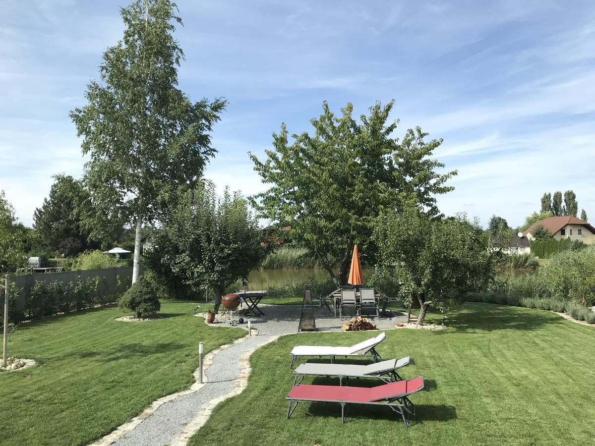 Dobre udržiavaná záhrada s trávnikom, stromami, ležadlami a stolom so slnečníkom.