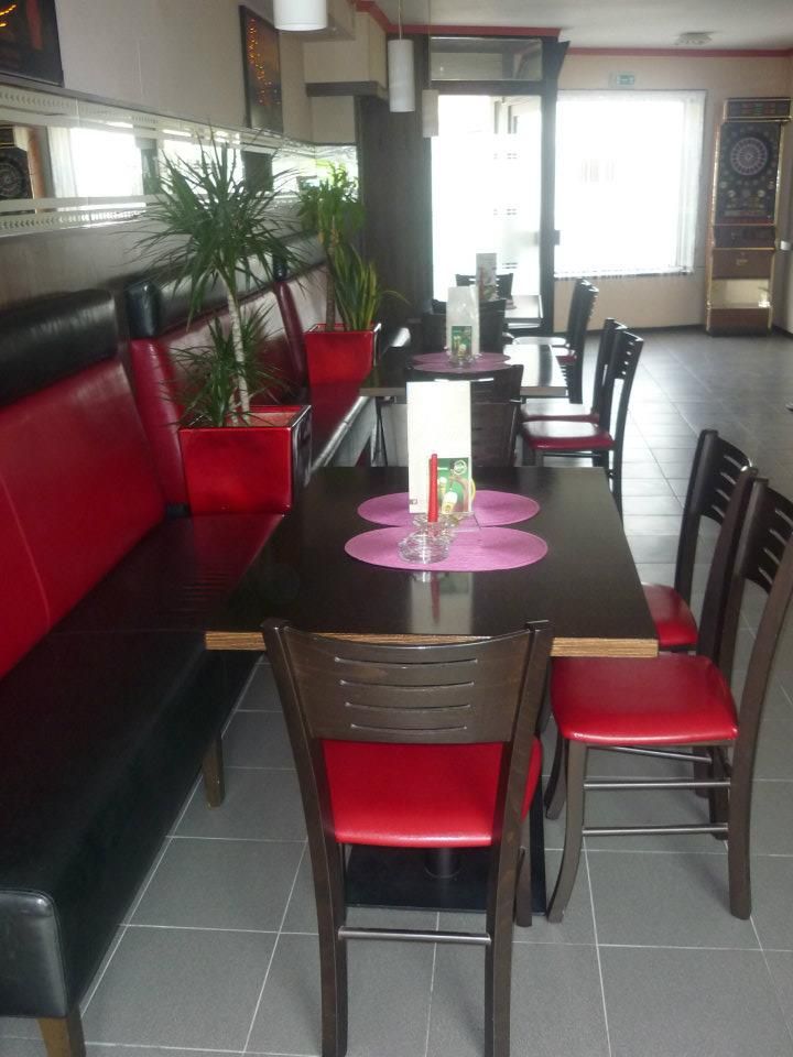 Pohľad do interiéru kaviarne s červeným a čiernym nábytkom, rastlinami a automatom na šípky.