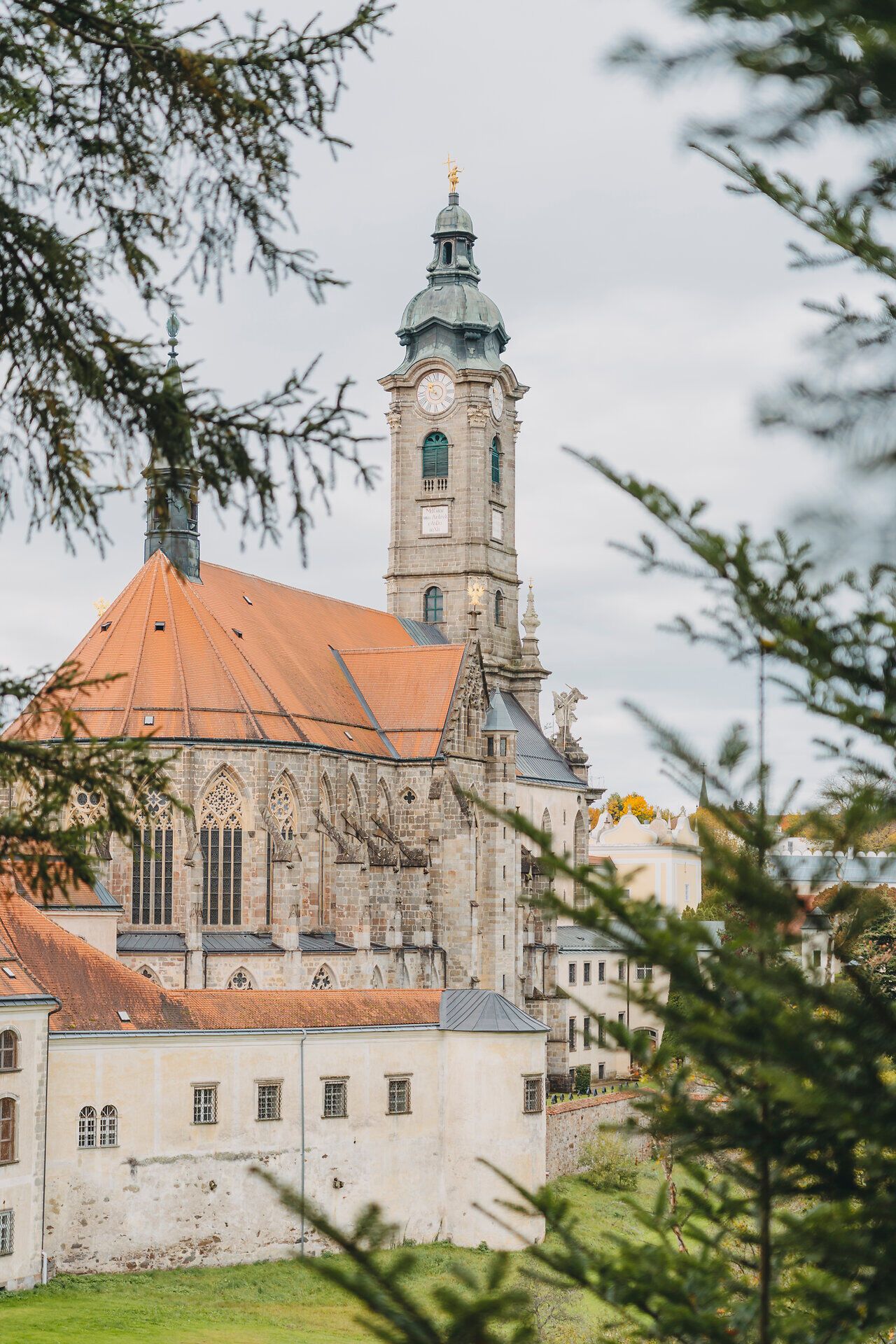 Die majestätische Architektur des Klosters erhebt sich zwischen den sanften Hügeln, umgeben von einer malerischen Herbstlandschaft. Die warmen Farben der fallenden Blätter schaffen eine einladende Atmosphäre, die zum Verweilen einlädt. Ein Ort der Ruhe und Besinnung, ideal für Naturliebhaber und Kulturinteressierte.