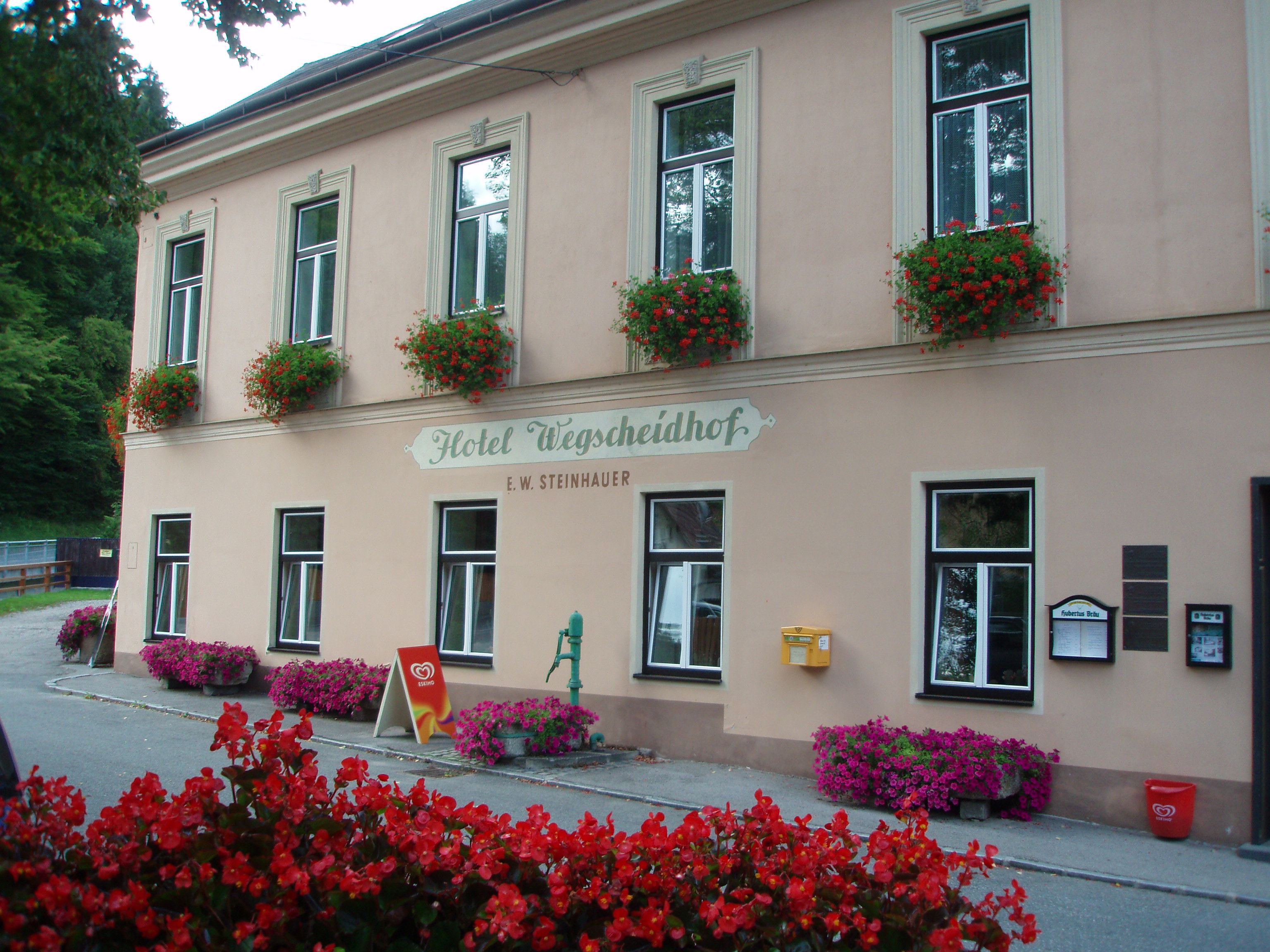 Fasáda hotela Wegscheidhof s kvetinovými truhlíky a nápismi.