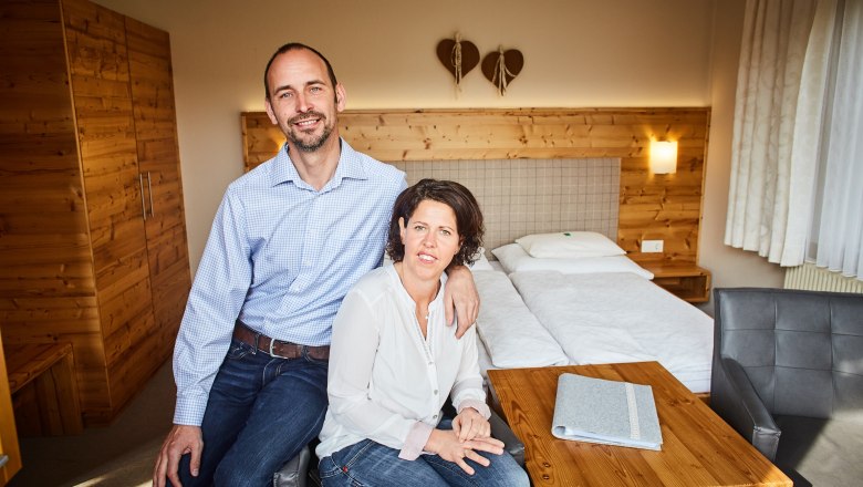 Pár sedí v útulnej izbe s dreveným nábytkom a manželskou posteľou.