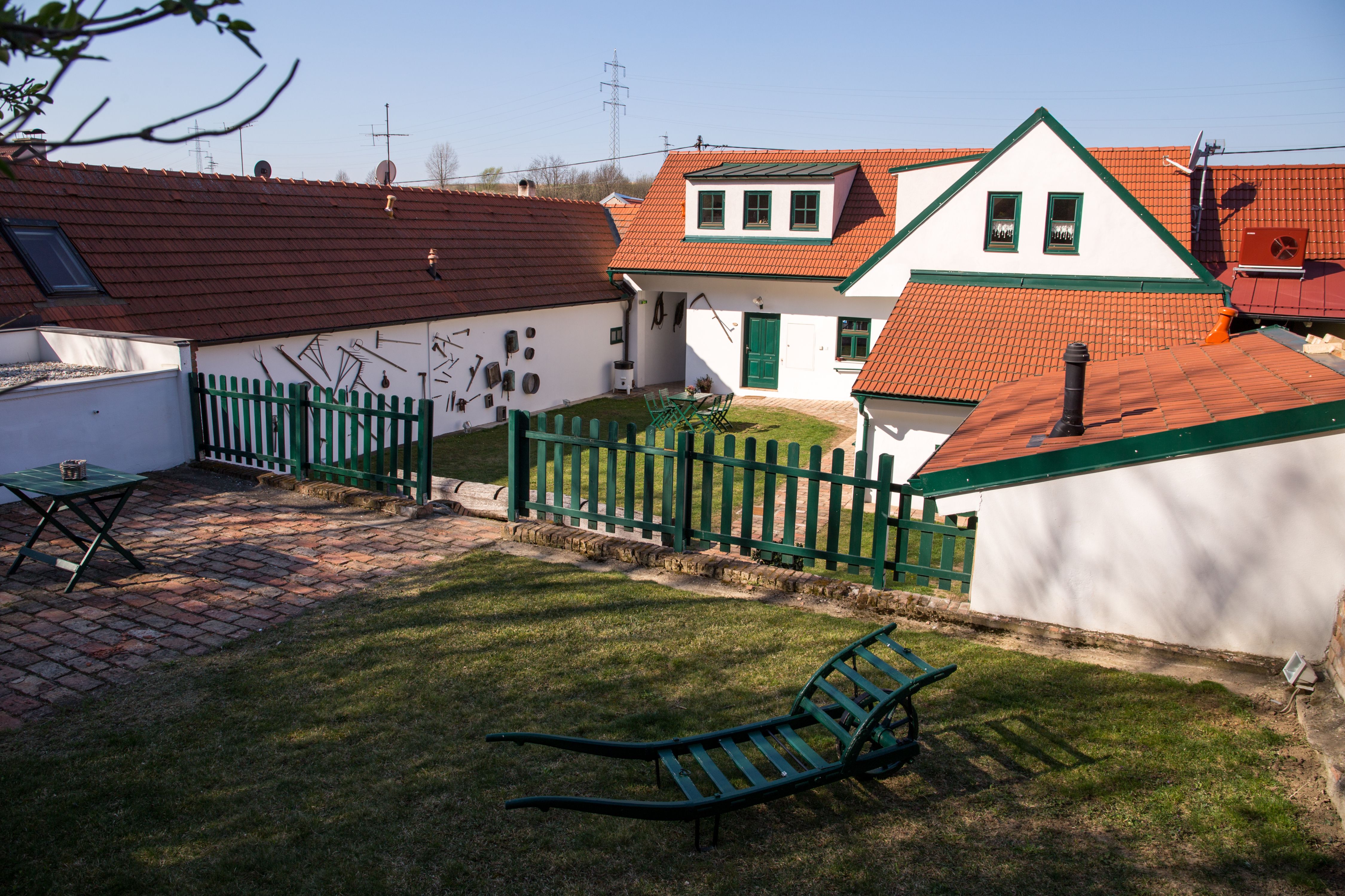 Tradičná vinica s červenými škridlovými strechami, zeleným plotom a záhradným nábytkom na lúke.