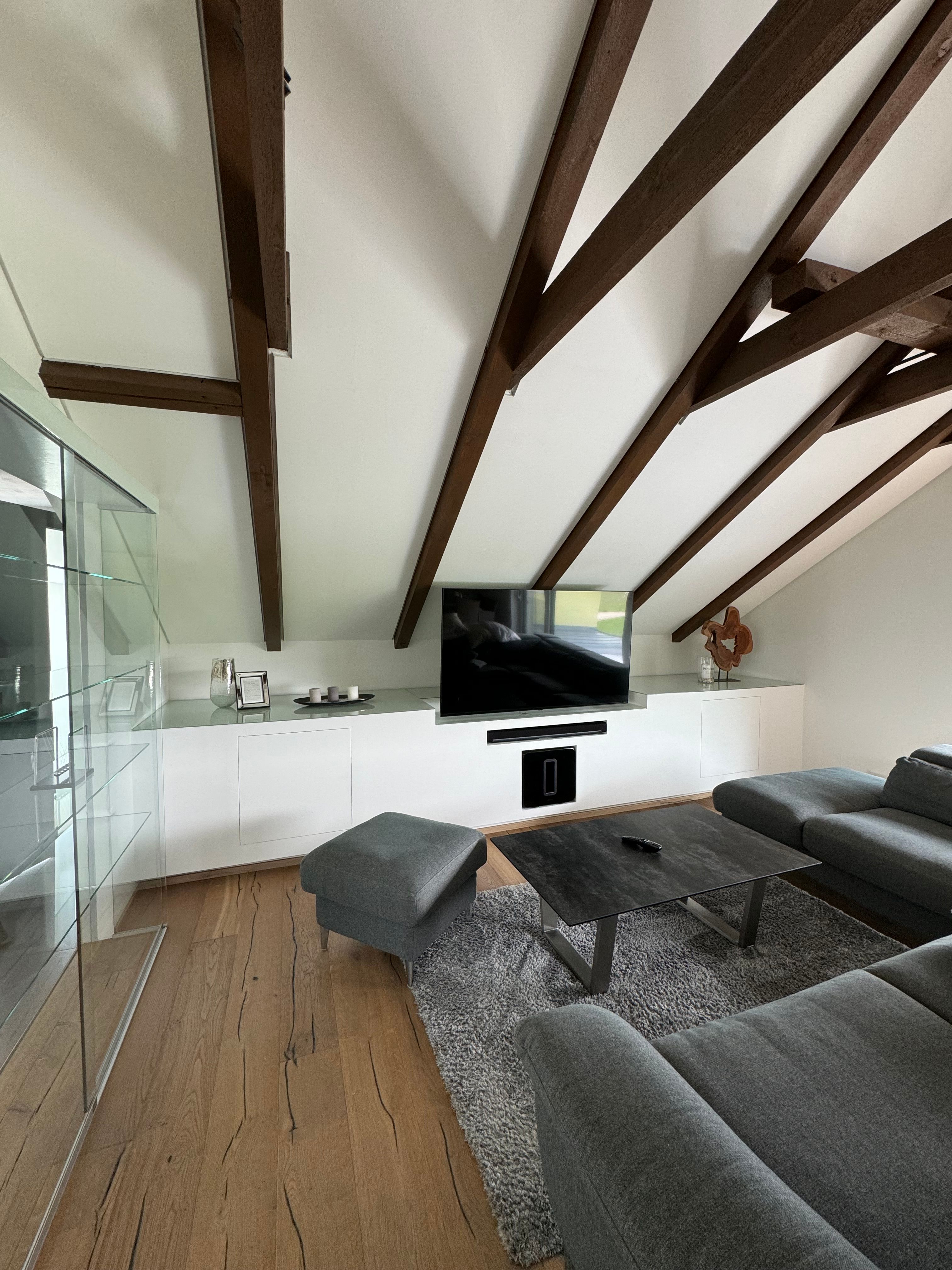 Moderný obývací priestor so sivou pohovkou, dreveným trámovým stropom a TV s plochou obrazovkou.
