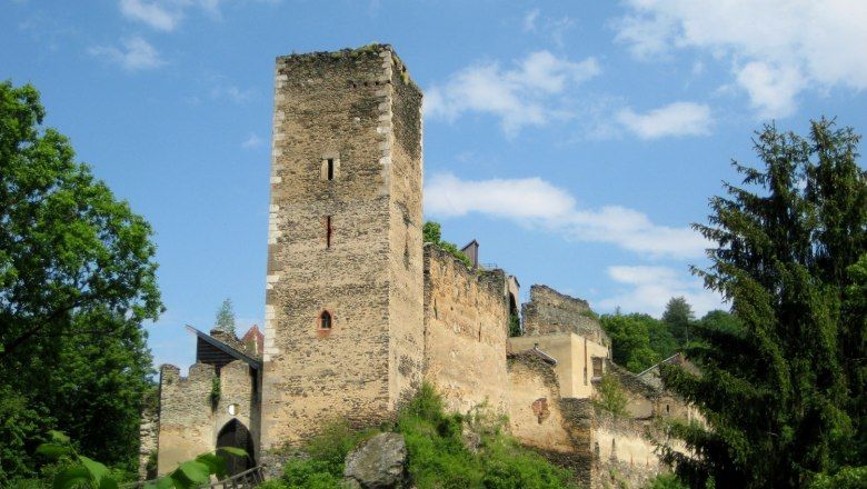 Zrúcaniny hradu Kaja obklopené stromami a pod modrou oblohou.